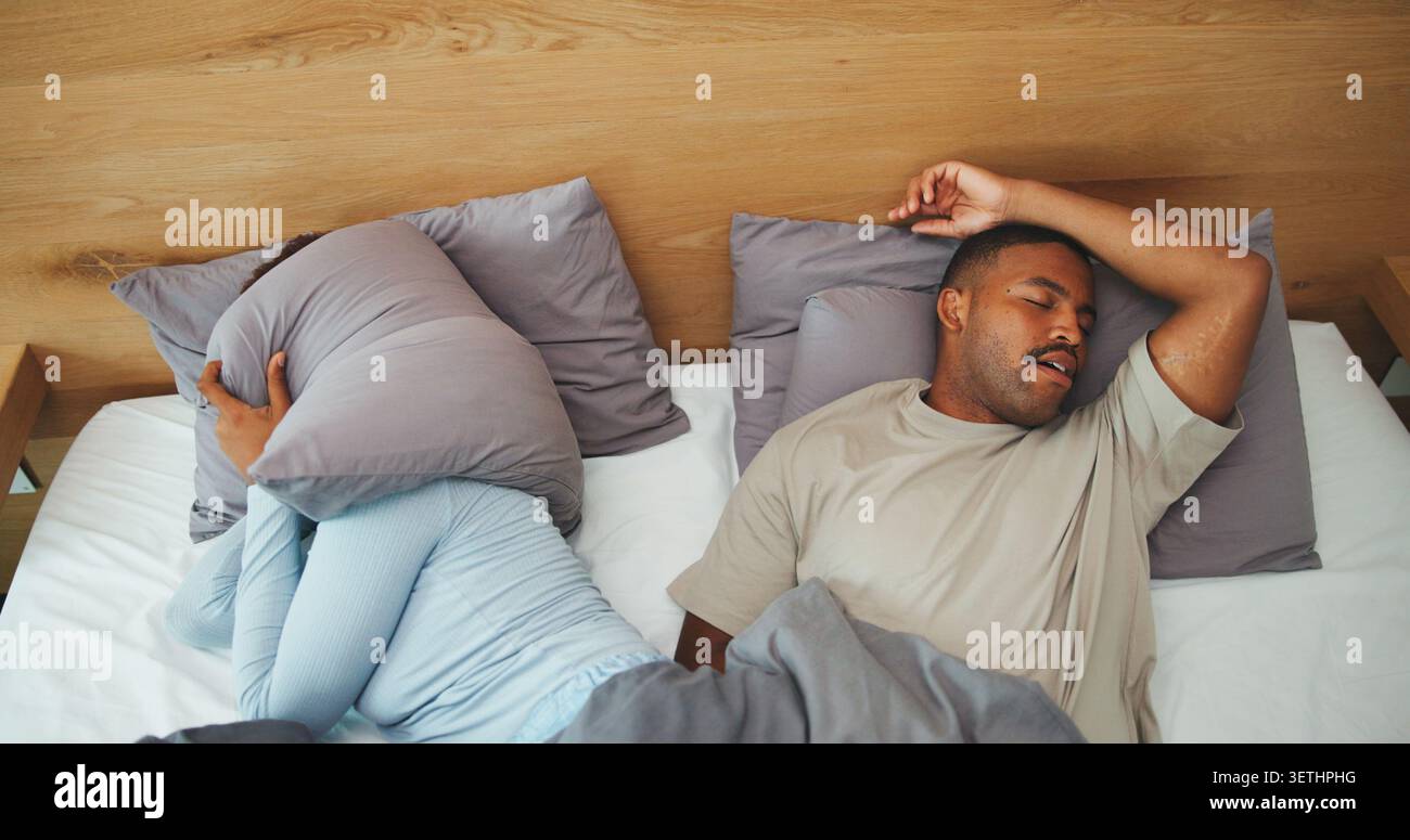 Russante, coppia e donna con un cuscino nel letto per disturbare, rumore e infastiditi per l'apnea del sonno. Casa, sopra e le persone coprono le orecchie in camera da letto con Foto Stock