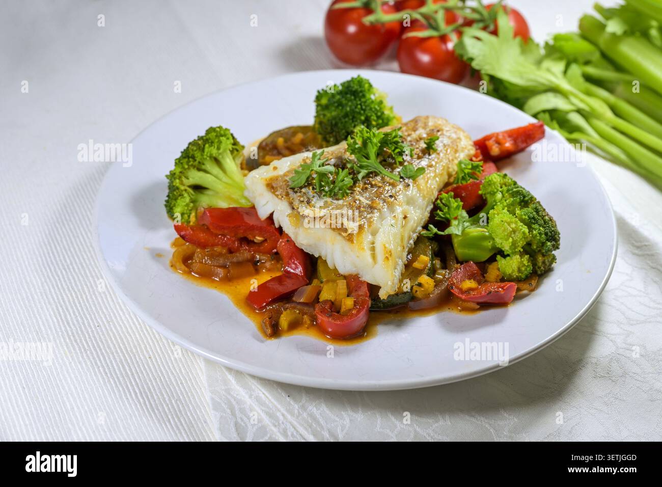 Filetto di pesce di merluzzo su verdure colorate come peperone rosso, broccoli, zucchine, sedano e prezzemolo guarnire su un piatto bianco, pasto sano, c Foto Stock