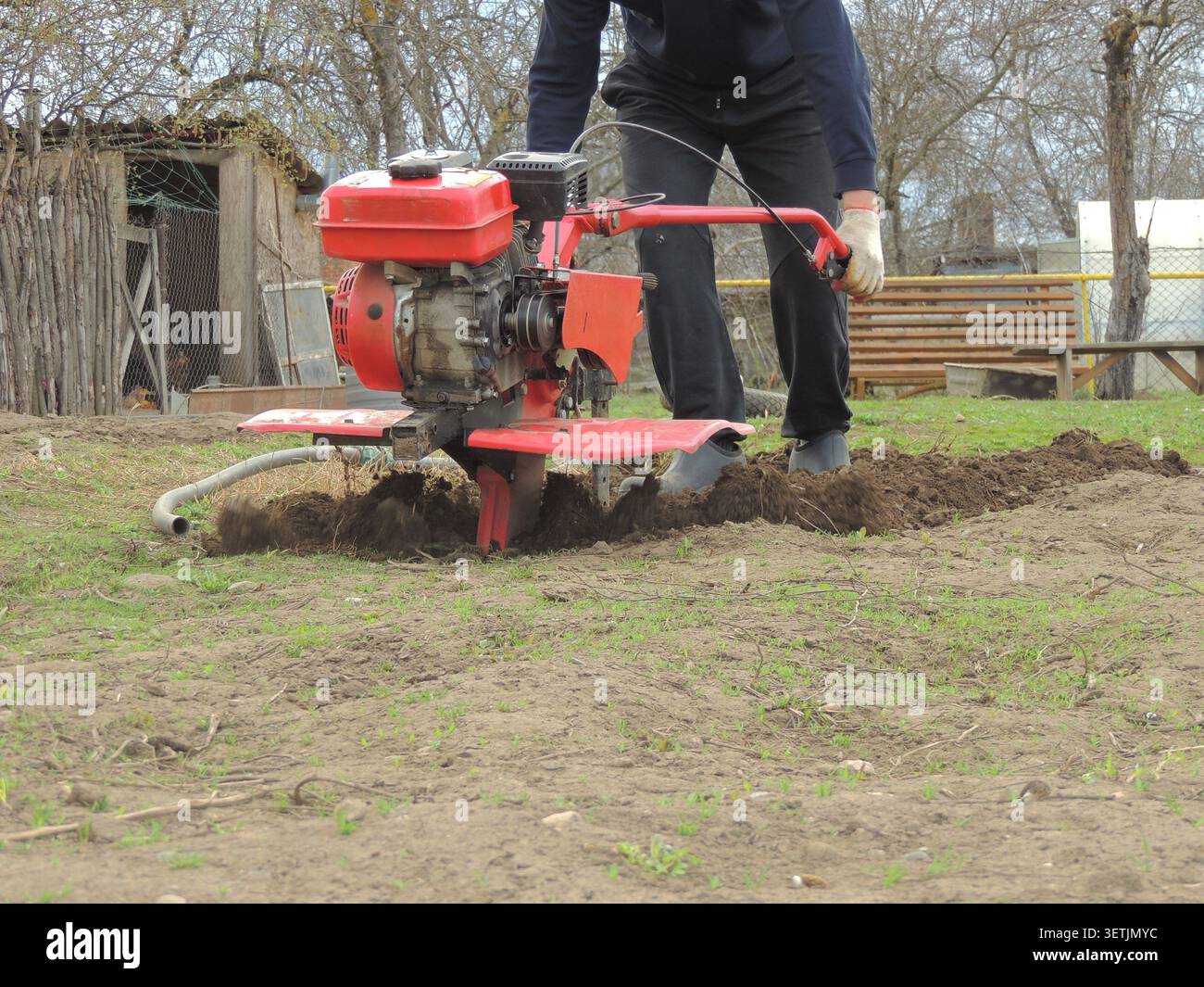 Il processo di dissodamento primaverile in un giardino o in un terreno di dacia utilizzando attrezzature da giardinaggio. Un agricoltore si trova dietro un trattore con operatore a terra Foto Stock