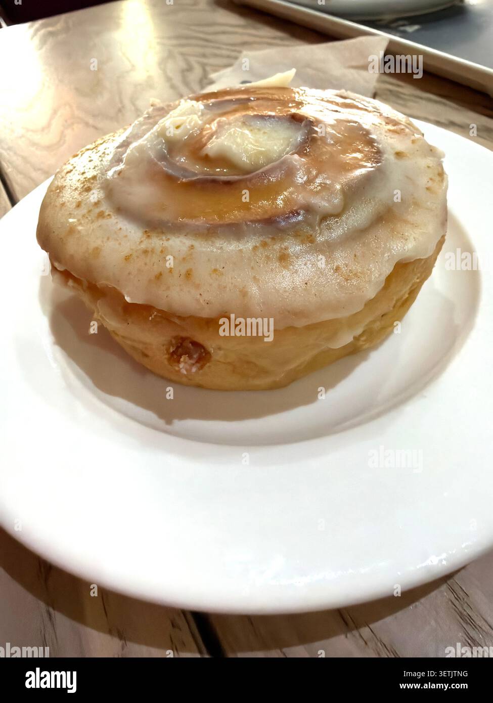 Involtino alla cannella con glassa bianca servito su un piatto all'interno di un caffè Foto Stock