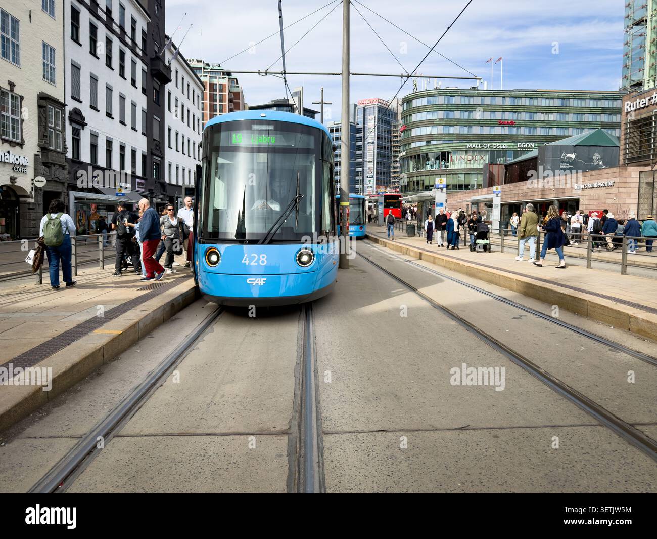 Tram blu CAF Urbos SL18 sui binari di Jernbanetorget a Oslo, Norvegia, con pedoni ed edifici cittadini sullo sfondo Foto Stock