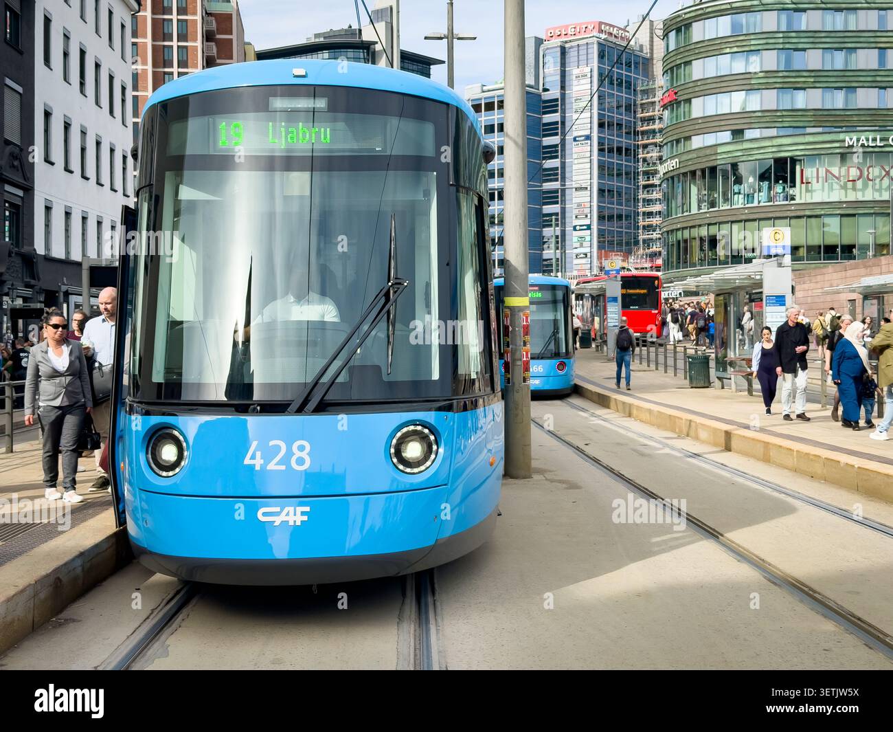 Tram blu CAF Urbos SL18 sui binari di Jernbanetorget a Oslo, Norvegia, con pedoni ed edifici cittadini sullo sfondo Foto Stock