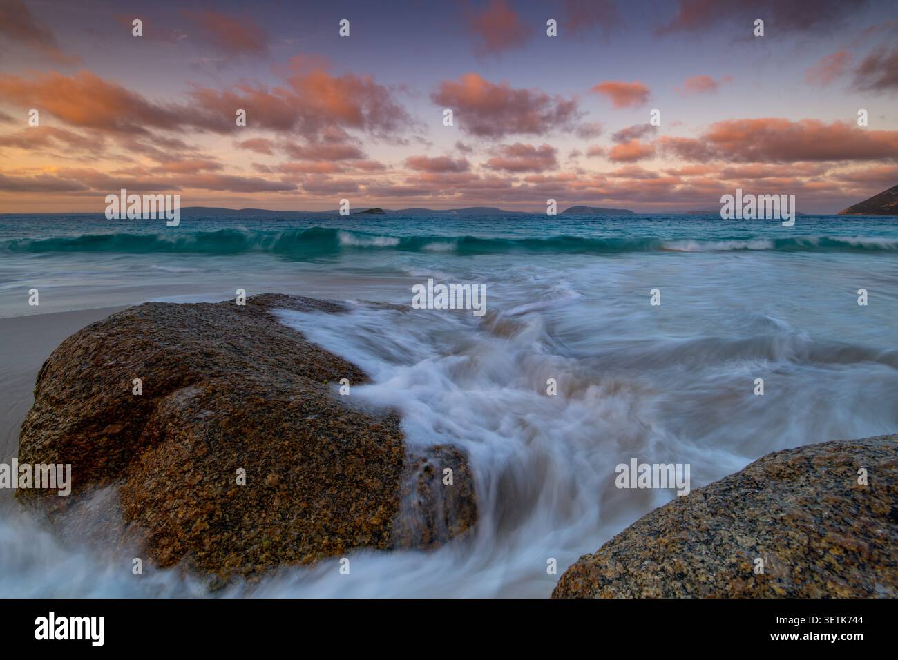 Vista di Misery Beach con massi di granito, onde dolci che si lavano sulla sabbia e un colorato cielo al tramonto sull'Oceano meridionale a Torndirrup, Weste Foto Stock