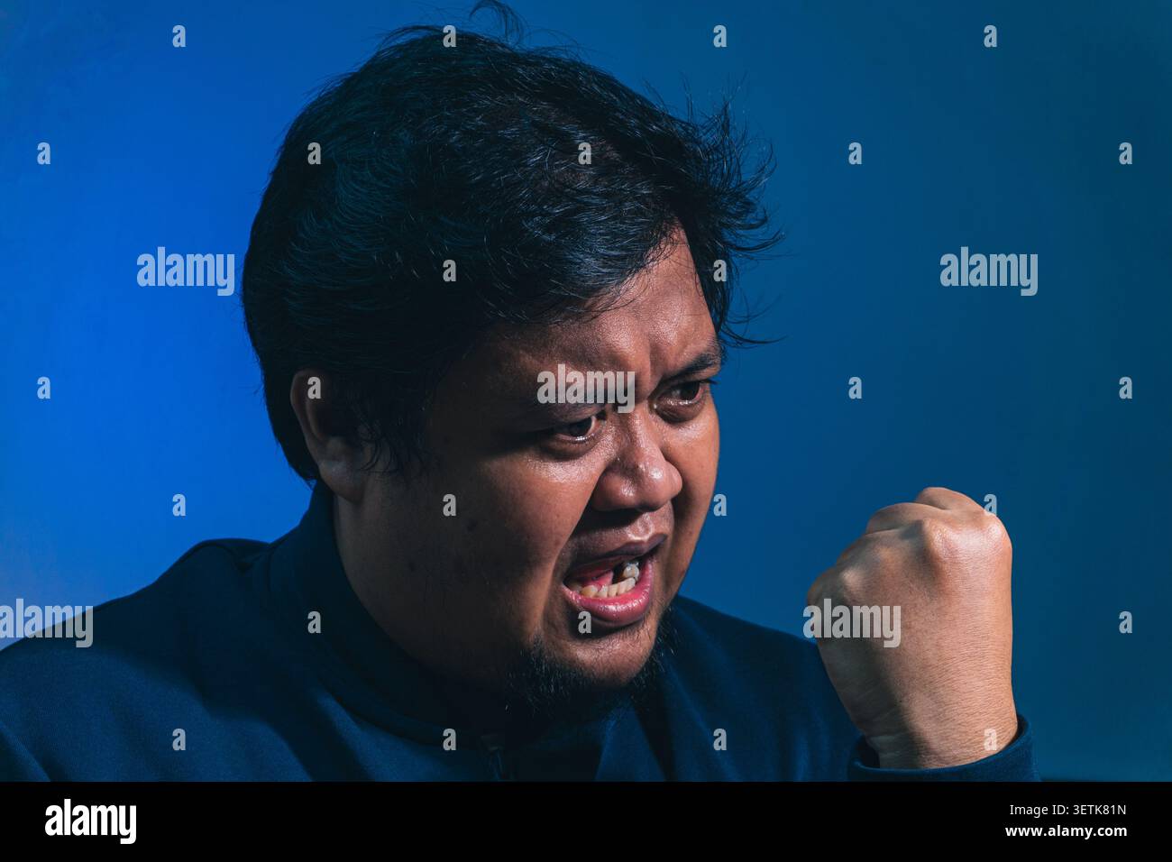 Un soggetto adulto di sesso maschile arrabbiato brilla bruscamente a fianco con un'espressione furiosa e un pugno alzato, mostrando emozioni aggressive, profonda frustrazione e dentro Foto Stock
