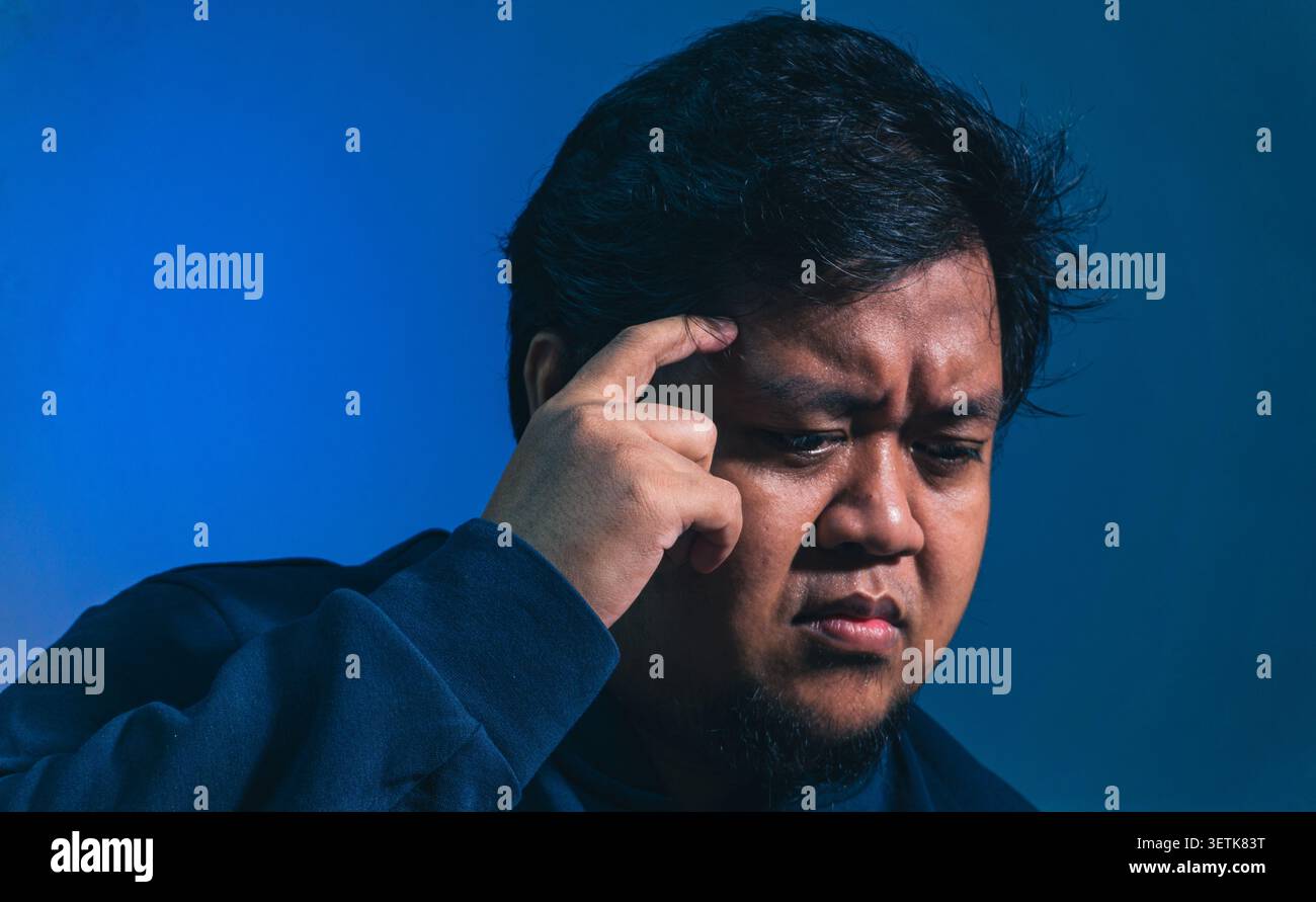Un soggetto adulto di sesso maschile mette un dito contro il tempio mentre guarda verso il basso con un'espressione seria, indicando un pensiero profondo, intenso c Foto Stock
