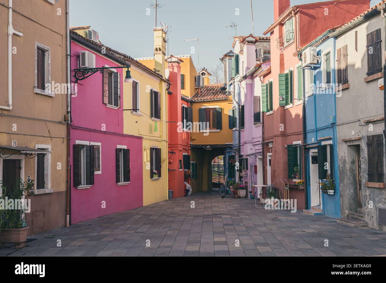 Vicolo vuoto e stretto circondato da case colorate di rosa, giallo e blu in una giornata di sole a Burano, Italia. Foto Stock