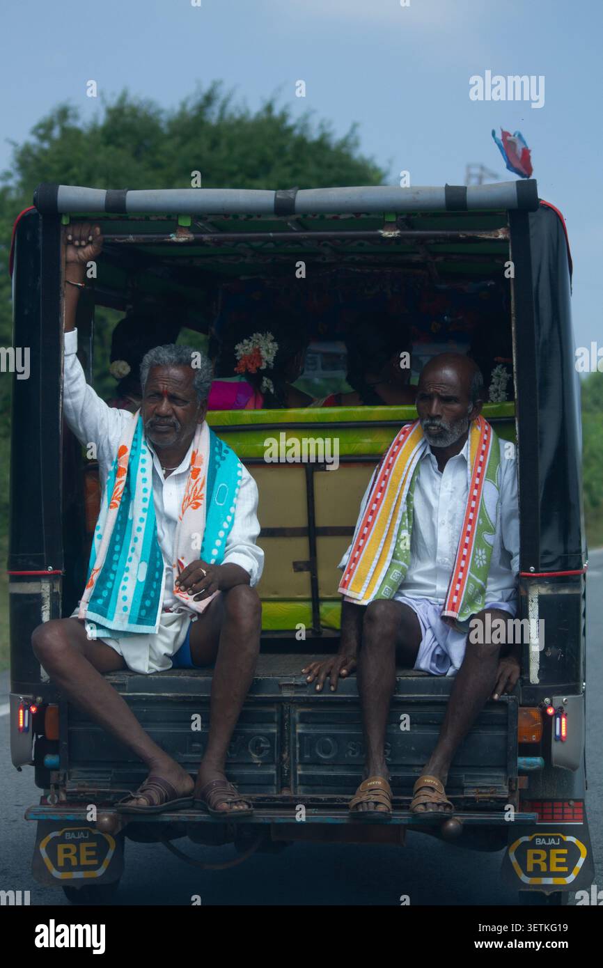Chikkaballapur, Karnataka, India - 10 dicembre 2023: Due uomini indiani in piedi sul retro di un camion che viaggiano attraverso la campagna Foto Stock