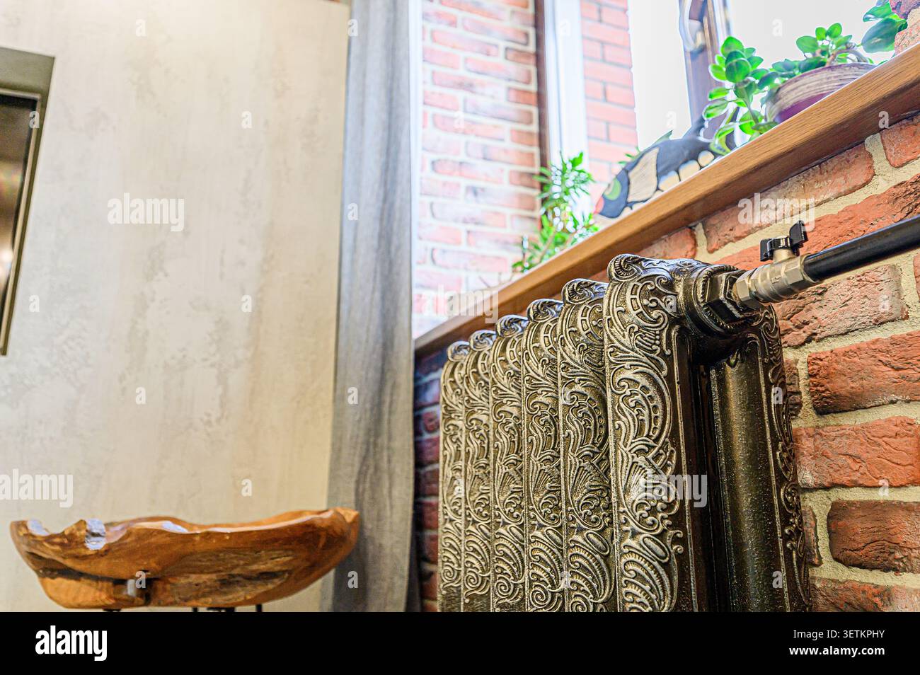 Camera d'epoca con radiatore decorativo in ghisa sotto una finestra e parete in mattoni sullo sfondo Foto Stock