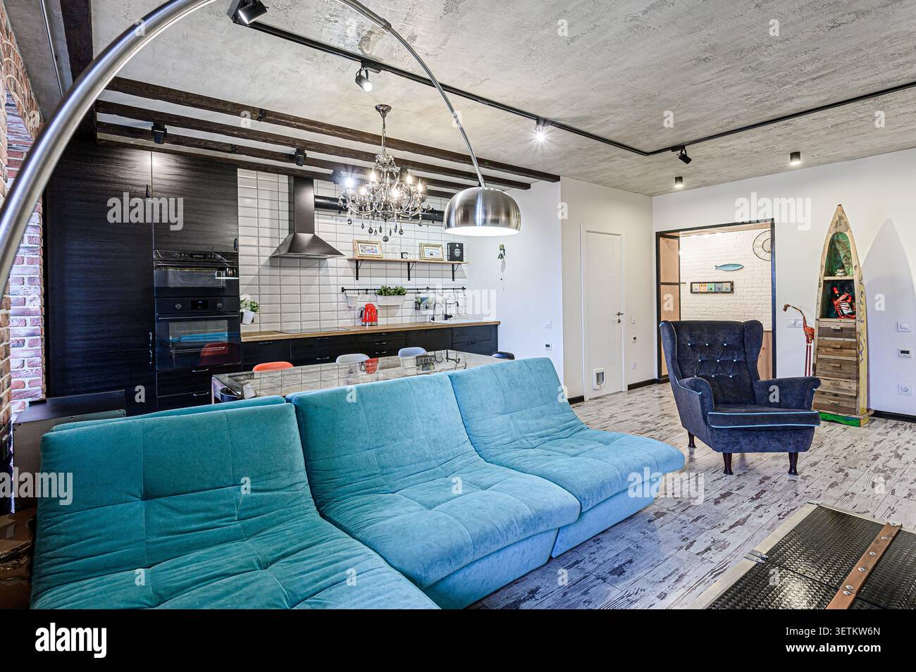 spazio abitativo contemporaneo con cucina a vista, con divano color tè, accenti di legno scuro e un mix di illuminazione industriale ed elegante Foto Stock