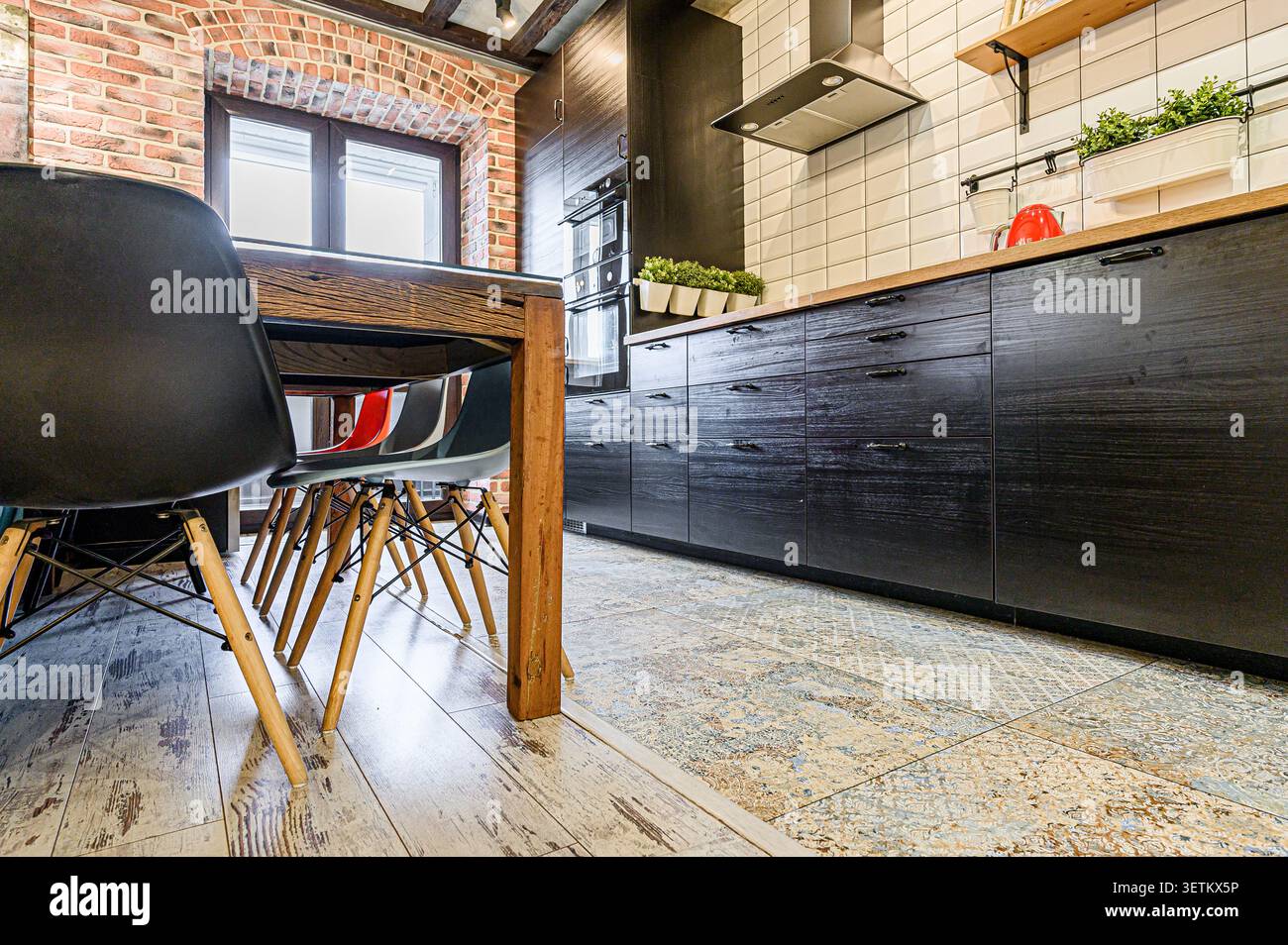 Cucina moderna con pareti in mattoni, armadi neri, tavolo in legno e sedie. Design rustico-chic Foto Stock