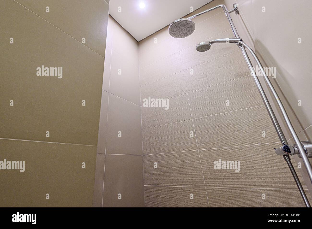 Doccia moderna con pareti in piastrelle beige e doccia cromata con due soffioni. Design pulito e contemporaneo Foto Stock