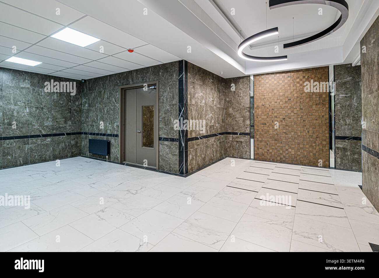 Lobby moderna con pareti effetto marmo, pavimenti in piastrelle bianche con accenti neri e lampade circolari uniche. La porta e le pareti a motivi geometrici aggiungono un tocco visivo Foto Stock