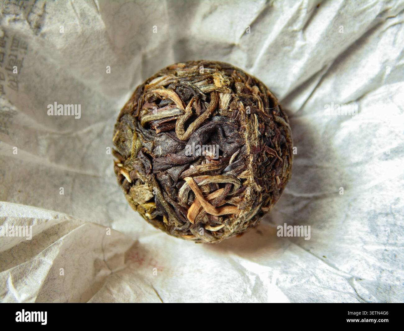 Palla da tè PU-erh cinese su carta da imballaggio decorativa. Tradizionale prodotto di tè fermentato con autentico aspetto artigianale. Foto Stock