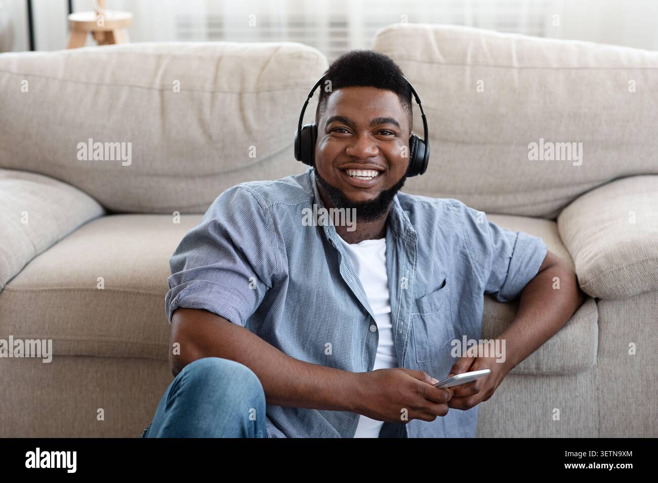 Musica di ascolto positiva dell'African Guy con cuffie e smartphone a casa Foto Stock