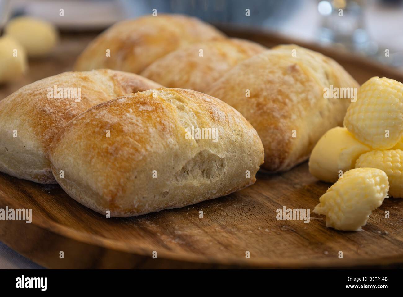 Panini di pane dorato appena sfornati serviti su un vassoio di legno con burro in occasione di un evento speciale. Foto Stock