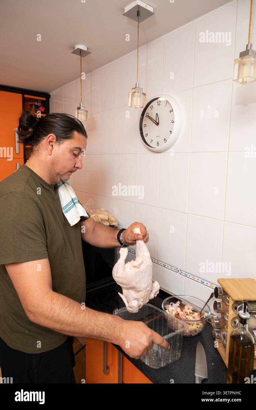 Uomo che tiene un pollo intero crudo in una cucina, pronto a cucinare la cena Foto Stock