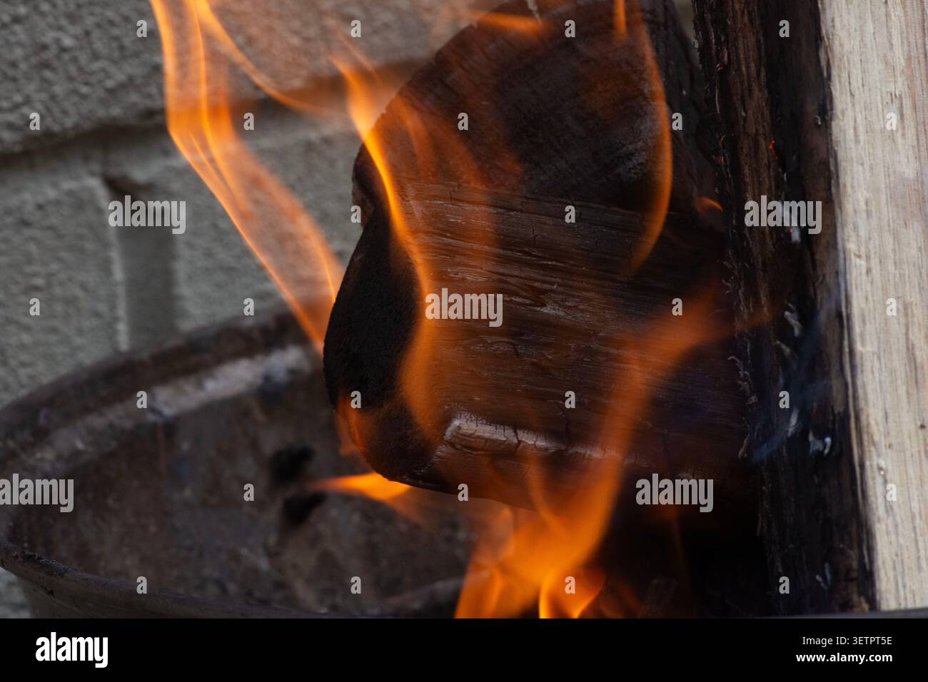 Una fotografia ravvicinata di fiamme arancioni brillanti che si innalzano su uno sfondo scuro, mostrando texture dettagliate del fuoco, brace incandescenti e calore intenso. Foto Stock