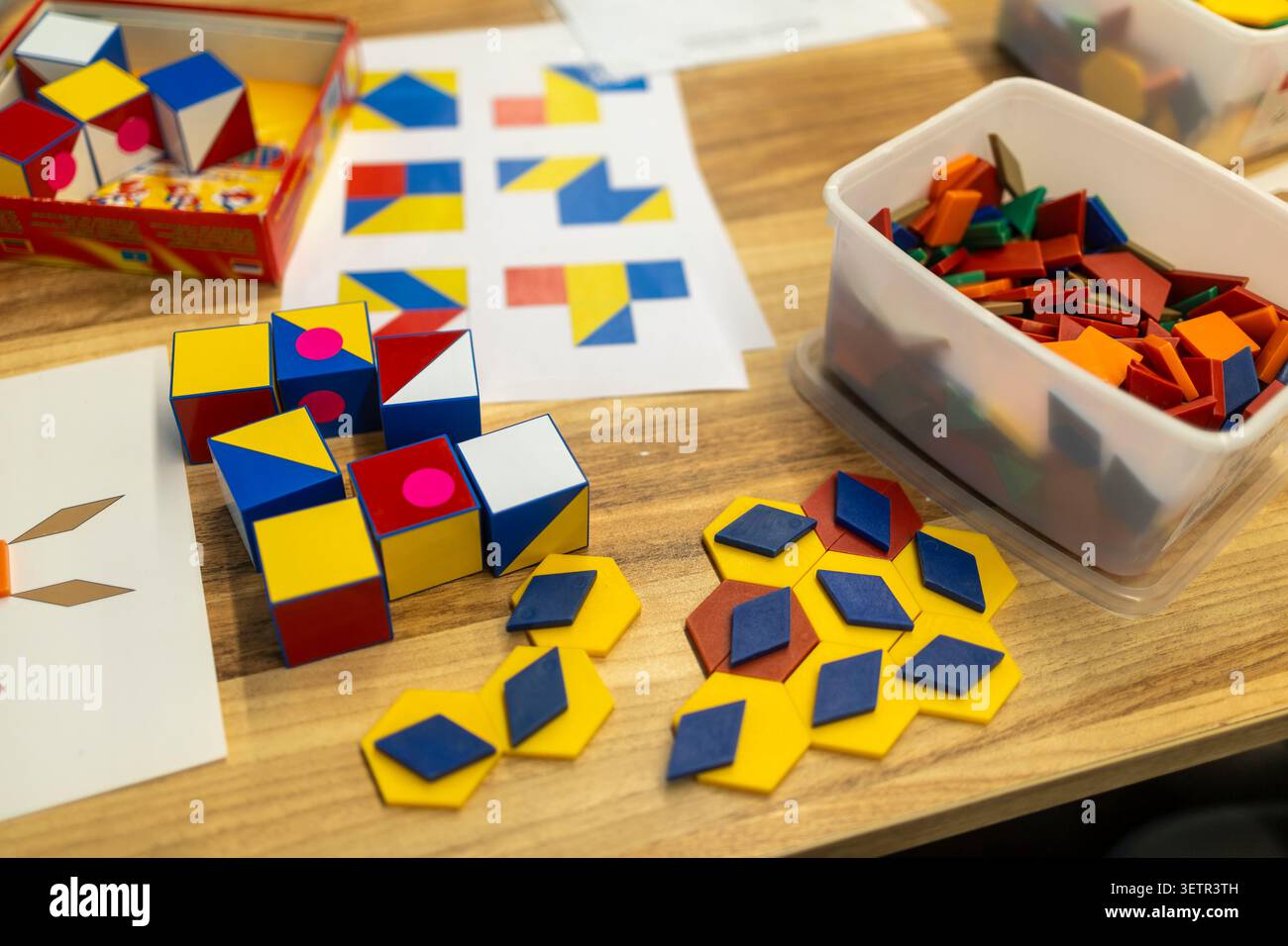 Primo piano di colorati cubi di puzzle logici in plastica e piastrelle geometriche piatte sparse su una superficie di un tavolo in legno durante un'attività didattica, con sor Foto Stock