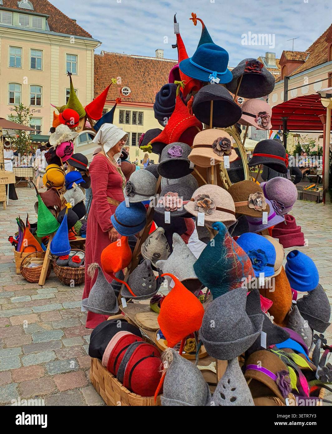 Tallinn, Estonia - 15 agosto 2020: Un venditore di costumi medievali si erge accanto a una colorata esposizione di cappelli in feltro fatti a mano in una bancarella del mercato durante il Talli Foto Stock