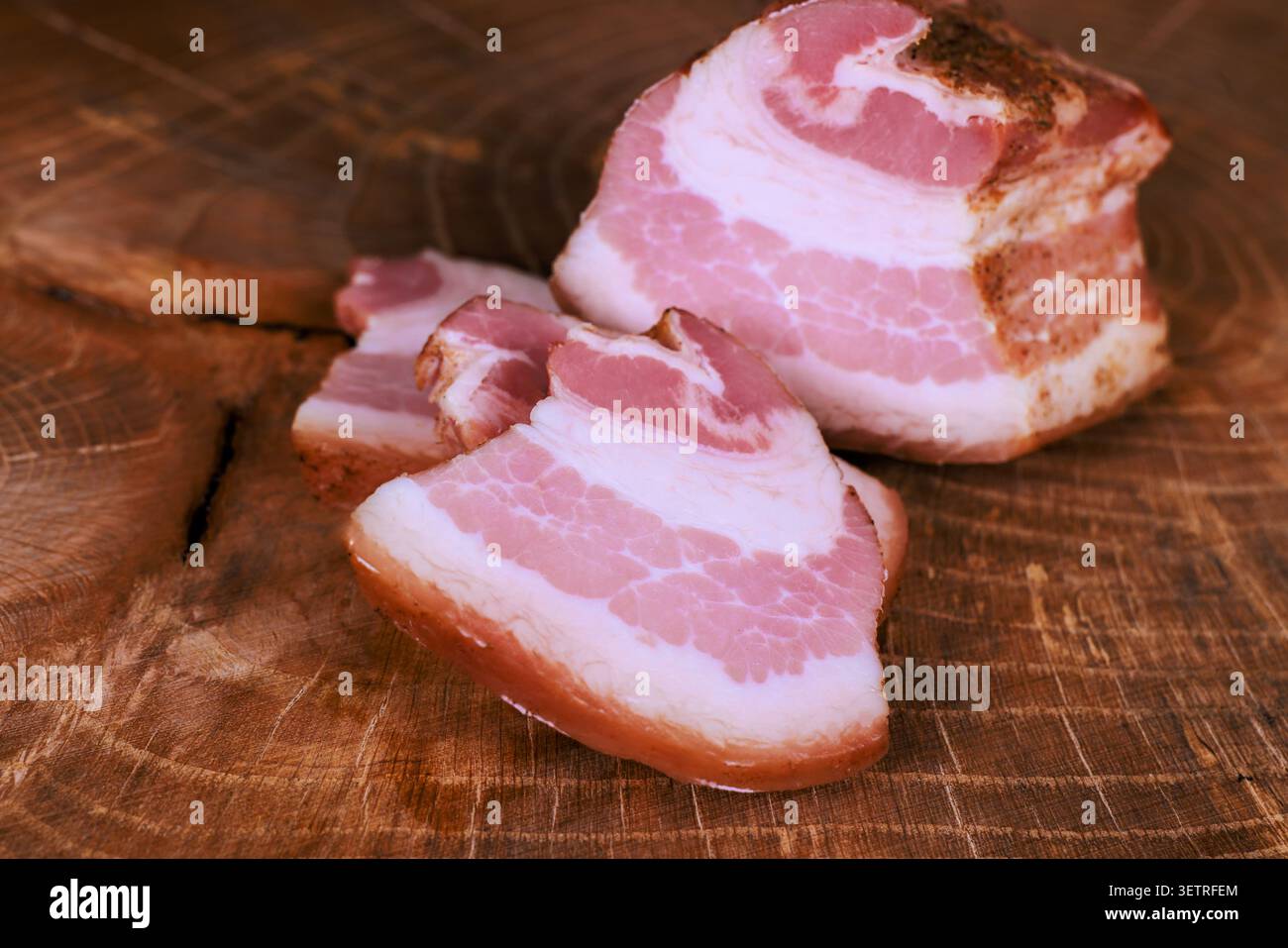 Le fette di pancetta poggiano su un grande tagliere in legno in un ambiente luminoso. Foto Stock