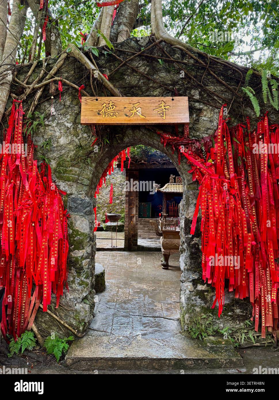 Arco in pietra del Tempio di Detian decorato con nastri rossi desideranti e preghiere scritte a mano, Cina - Immagine stock catturata con smartphone