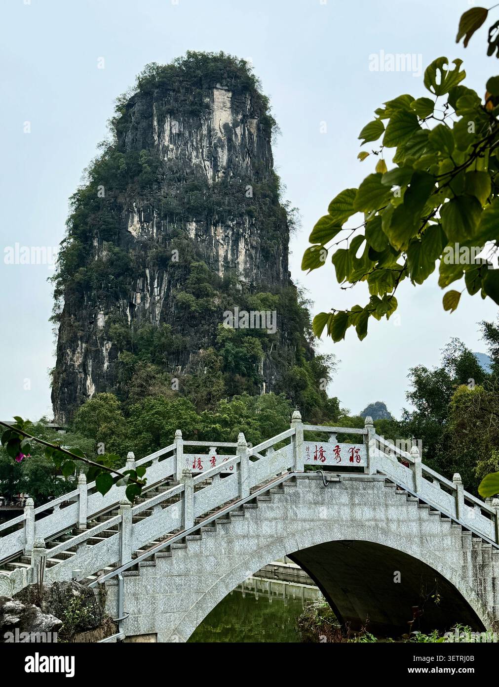 Tradizionale ponte ad arco di pietra con picco del Monte Carso a Yangshuo, Guangxi, Cina - Immagine stock catturata con smartphone
