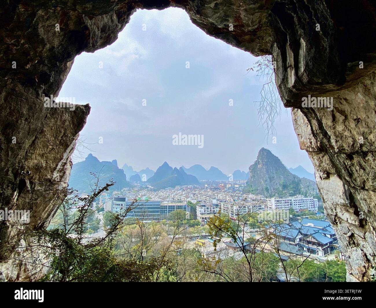 Una grotta di pietra calcarea naturale che si apre incorniciando una vista panoramica di una città moderna e delle montagne carsiche di Guilin Foto Stock