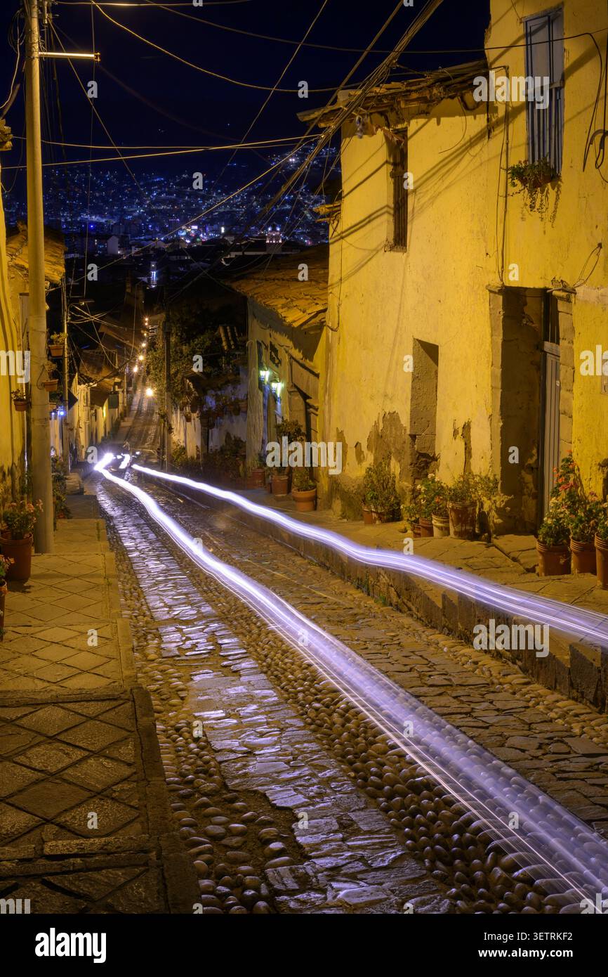 Strada notturna a Cusco, Perù, che sale su una ripida pendenza, con le luci di un'auto di passaggio. Foto Stock