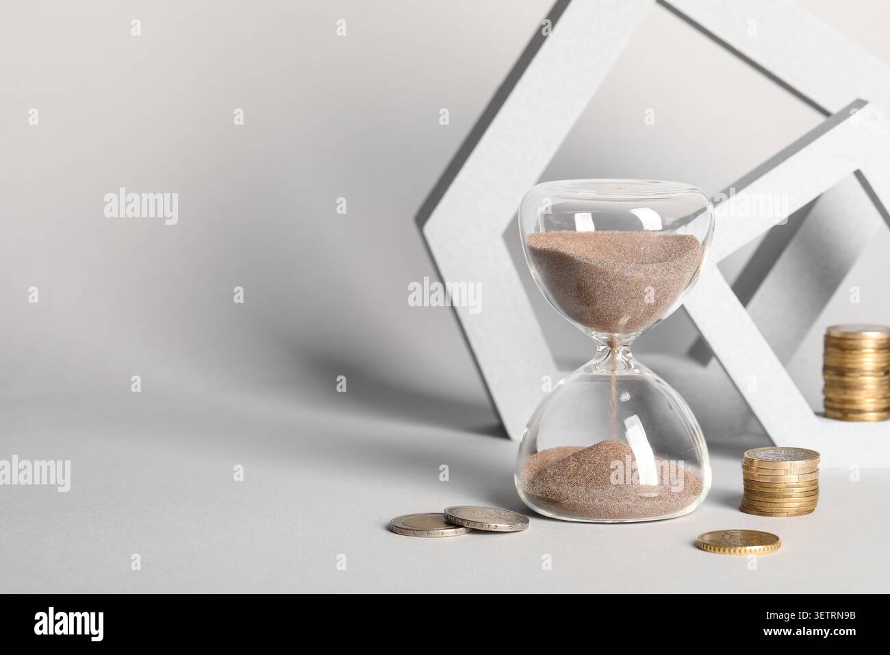 Clessidra con monete e forme geometriche su sfondo grigio Foto Stock