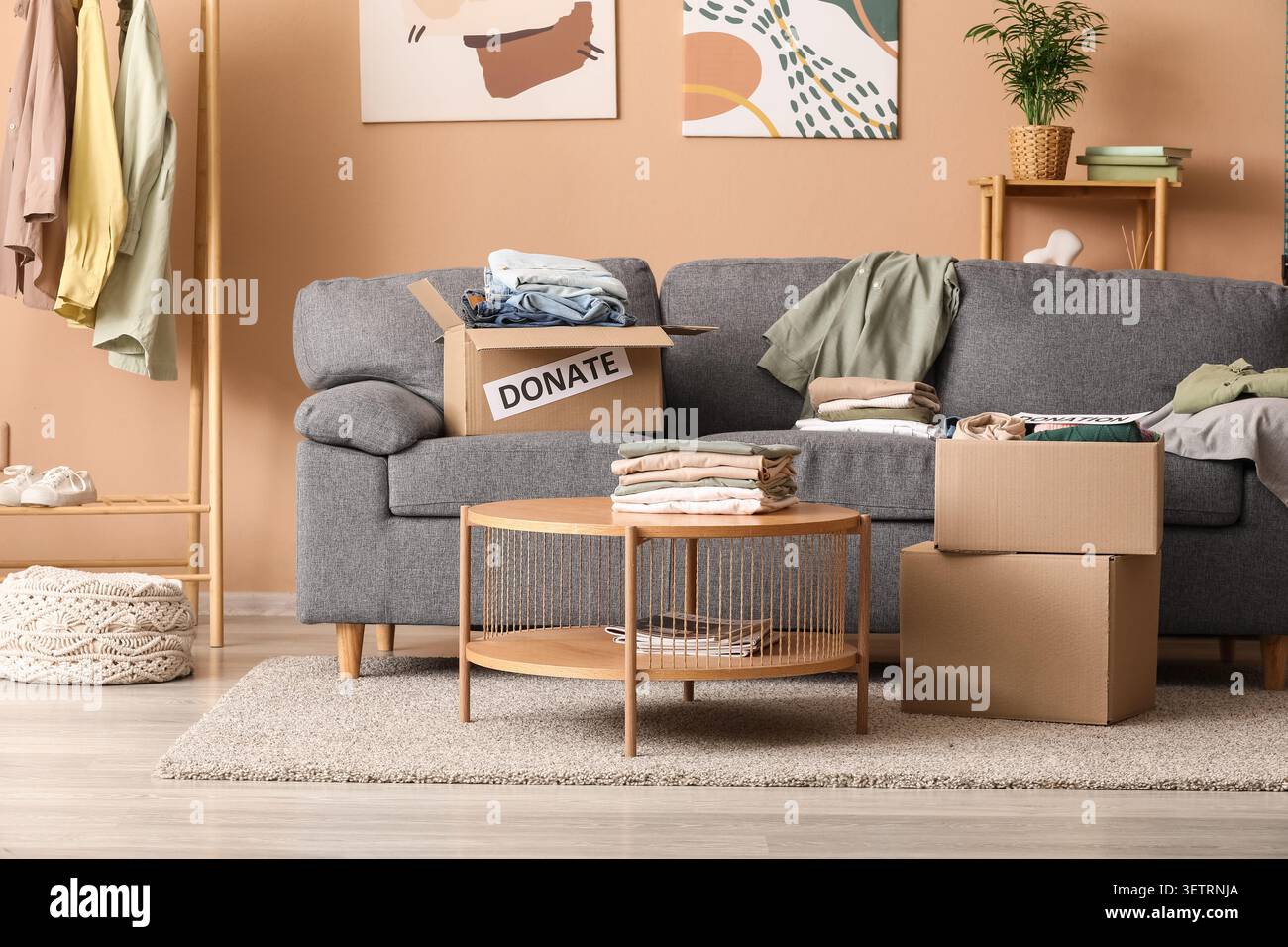 Scatole per donazioni di abbigliamento e abiti piegati in un accogliente salotto interno Foto Stock