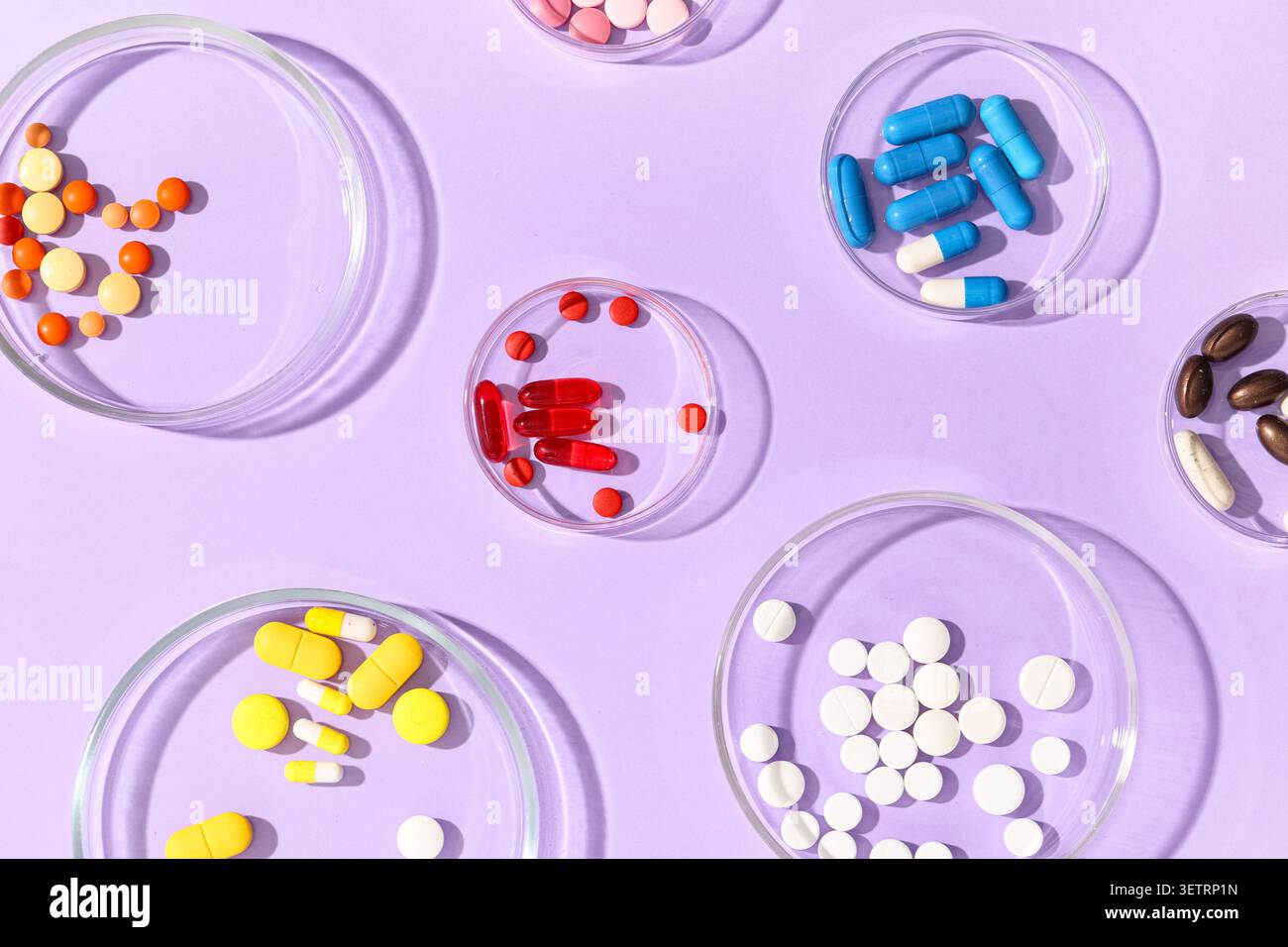 Varie pillole colorate e capsule in capsule Petri di vetro su sfondo viola Foto Stock