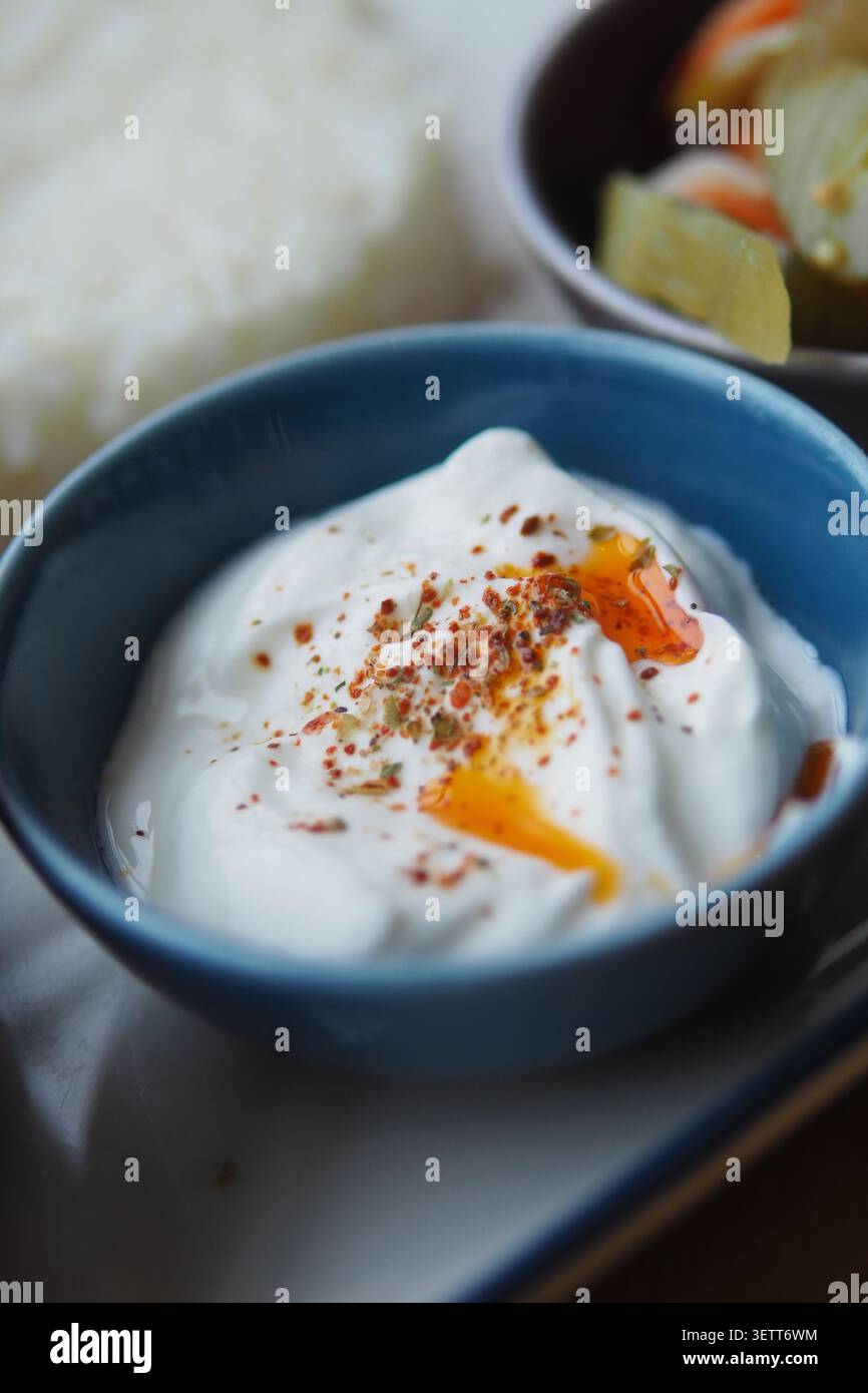 Recipiente di yogurt con spezie e olio su un piatto bianco Foto Stock