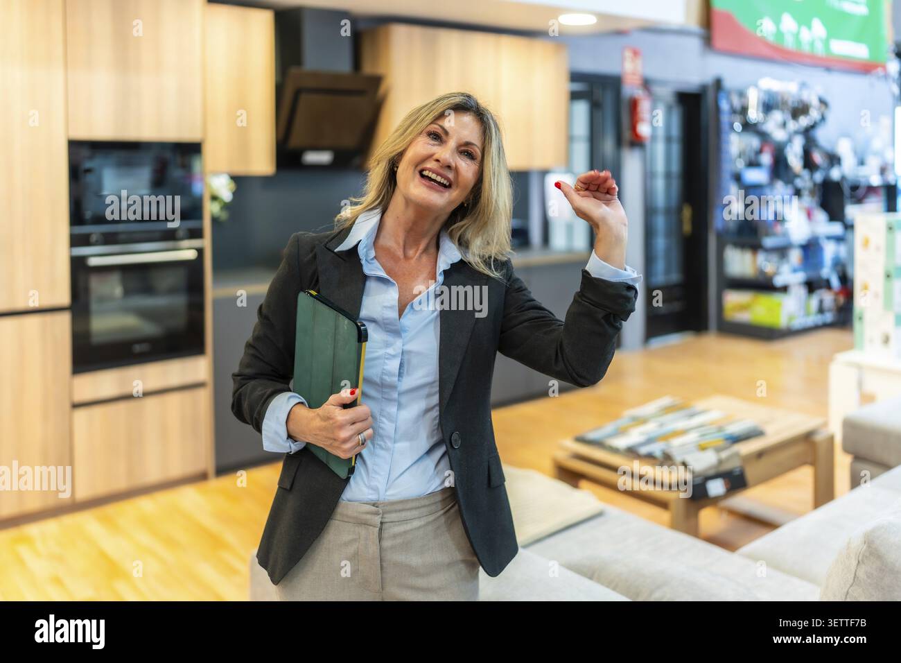 Consulente donna esperta in piedi in uno showroom moderno, tenendo in mano un tablet verde, sorridendo e gestendo mentre discute di miglioramento della casa e cucina Foto Stock