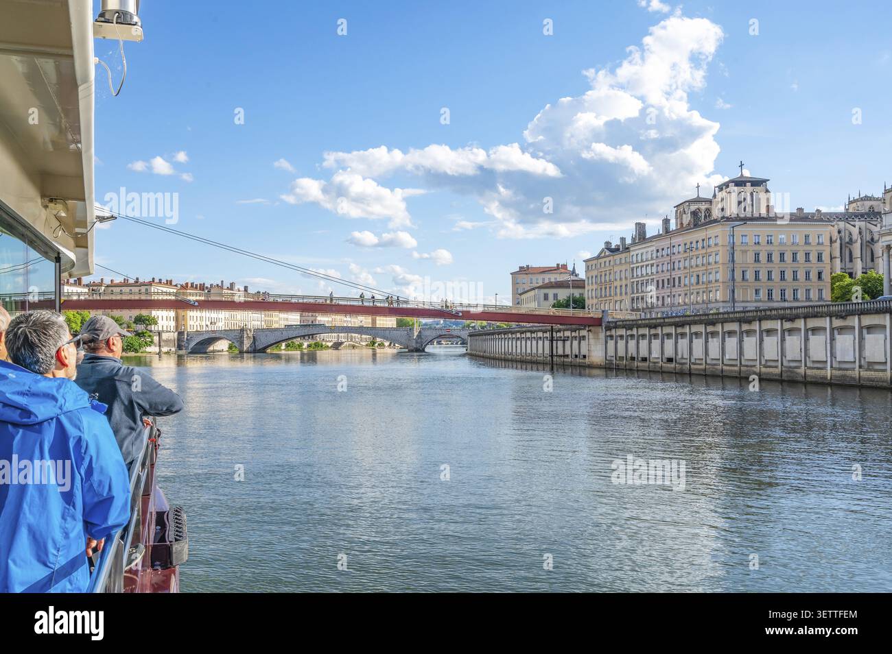 I turisti su una barca per escursioni ammirano la passerella pedonale rossa Passerelle Saint-Georges e Pont Bonaparte sul fiume Saone contro lo storico backdro Foto Stock