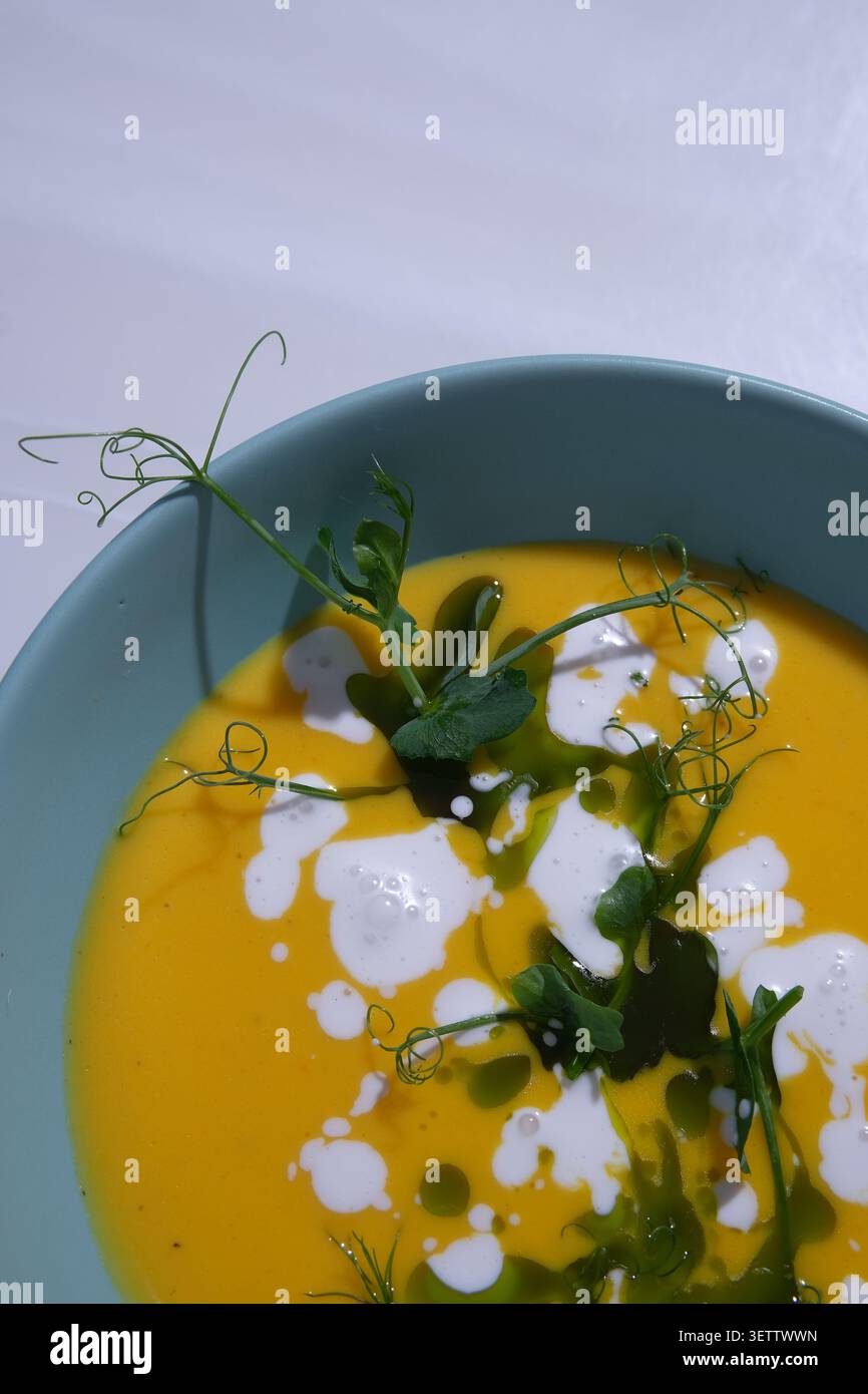 Elegante zuppa di verdure d'arancia in una ciotola blu con gocciolatoio di panna e germogli di pisello freschi Foto Stock