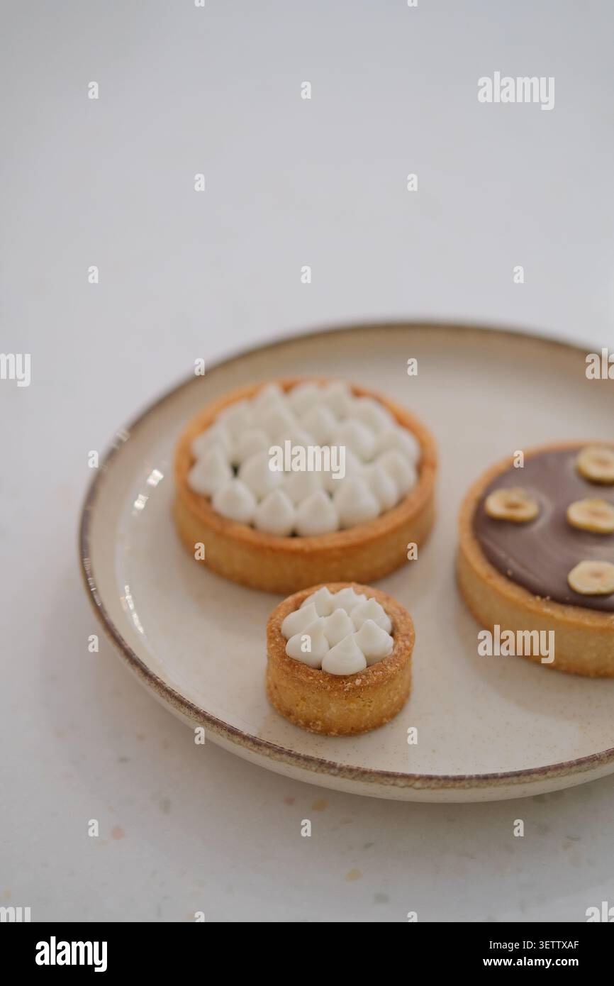 Piatto da dessert minimo con crostate assortite su un piano morbido e neutro Foto Stock