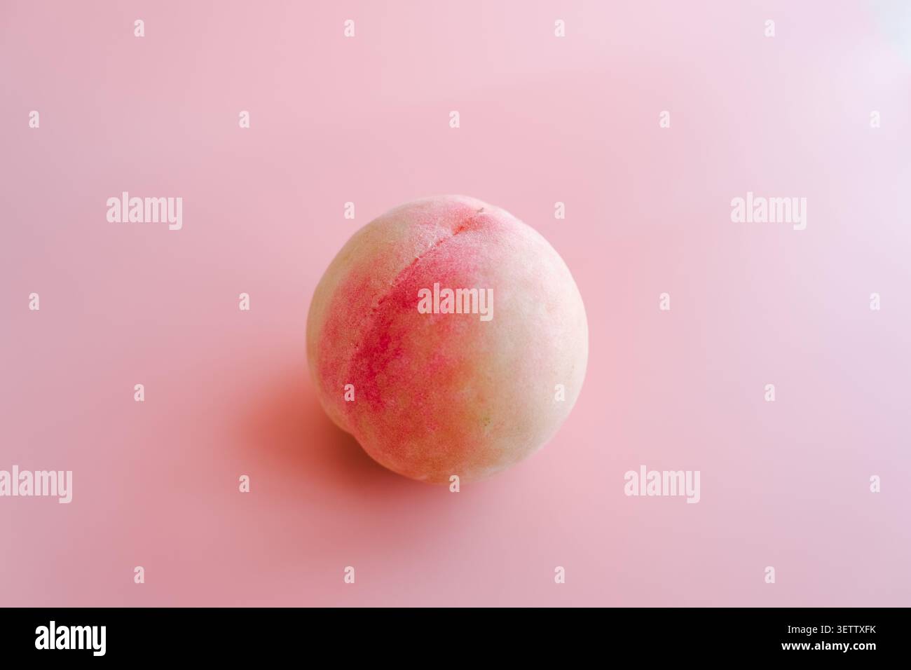 Pesca fresca singola su uno sfondo rosa tenue con luce e ombre delicate, frutta naturale con tonalità pastello e spazio di copia Foto Stock