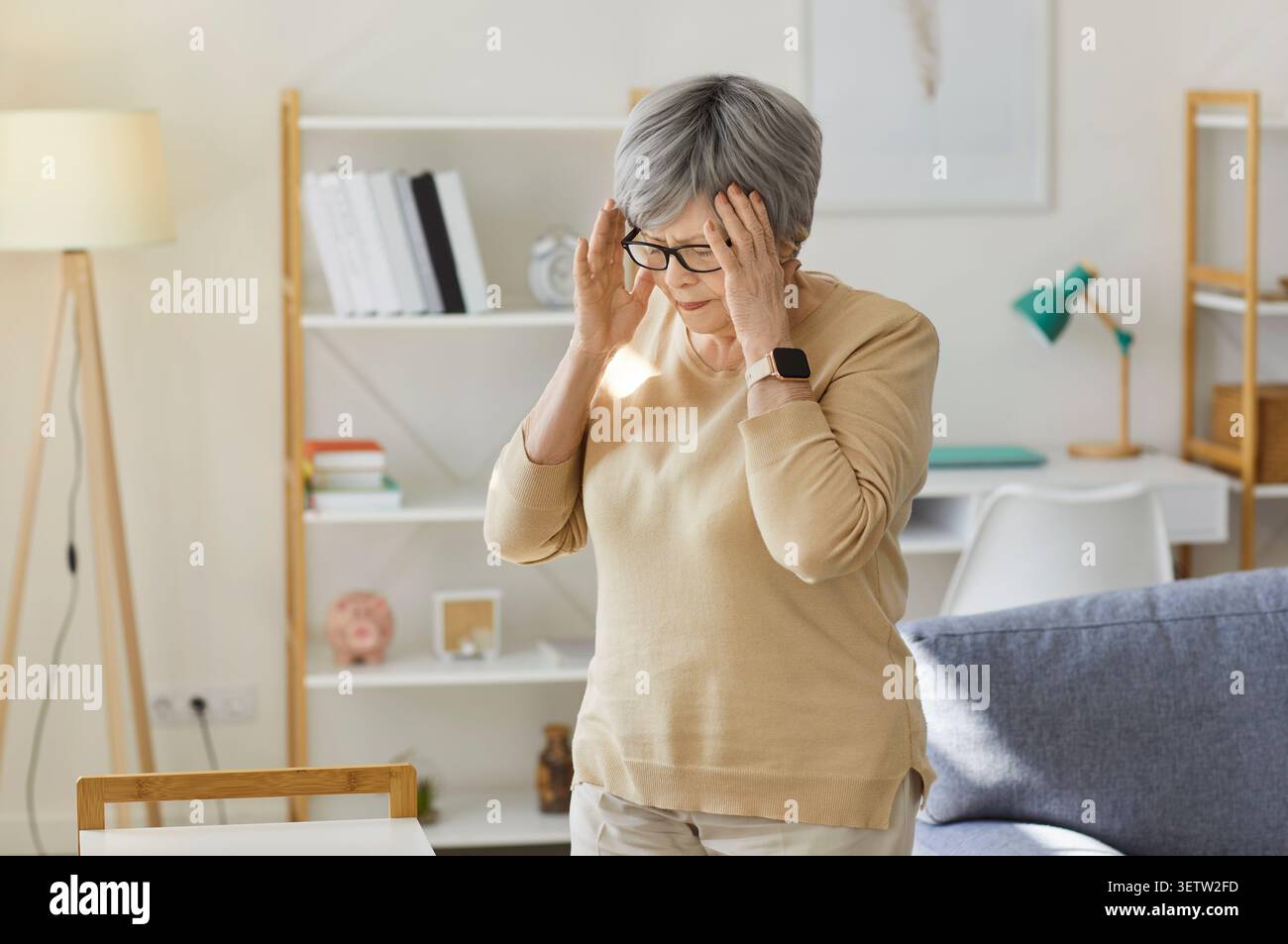 Donna anziana stressata in occhiali da vista in salotto a casa soffre di mal di testa Foto Stock