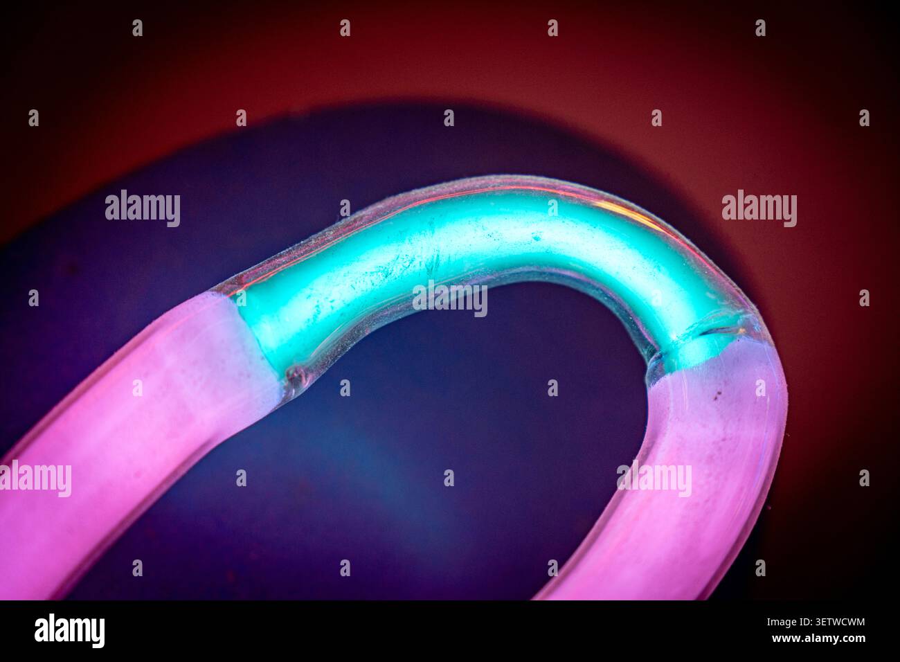 Tubo curvo in vetro al neon che illumina ciano e magenta su sfondo scuro con vignettatura Foto Stock