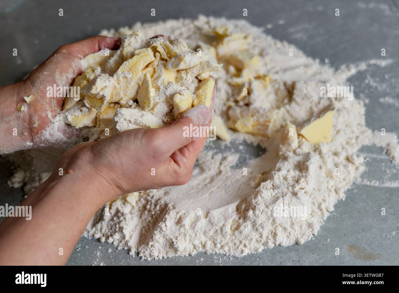 Le mani che sfregano il burro nella farina per preparare la briciola di pasta. Primo piano delle mani di un fornaio mescolando e strofinando pezzi freddi di burro con farina di grano bianco su una Foto Stock