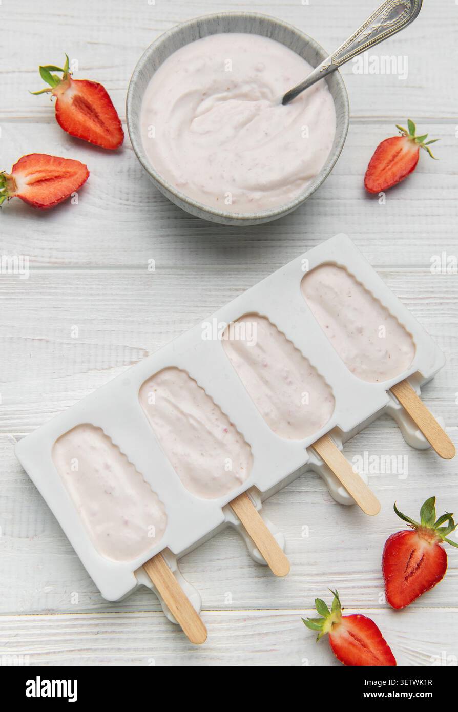 Lo yogurt alla fragola si prepara in muffa con frutti di bosco freschi e cremoso yogurt su un tavolo di legno Foto Stock