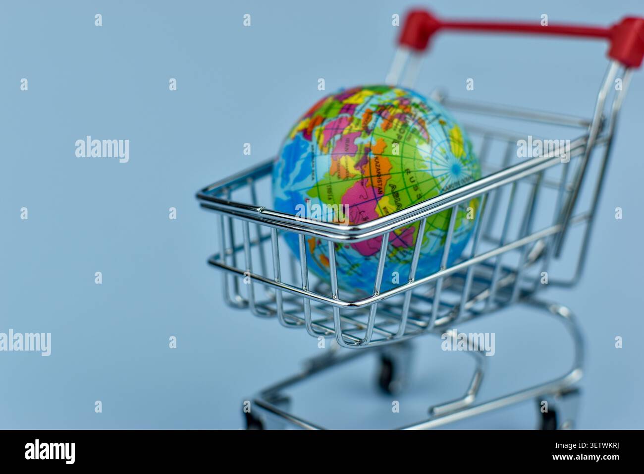 Il piccolo carrello può contenere globo. Una piccola casa si trova accanto al carrello. Sfondo blu, pulito, semplice. Commercio globale, commercio o concetto di mercato. Ideale per gli autobus Foto Stock
