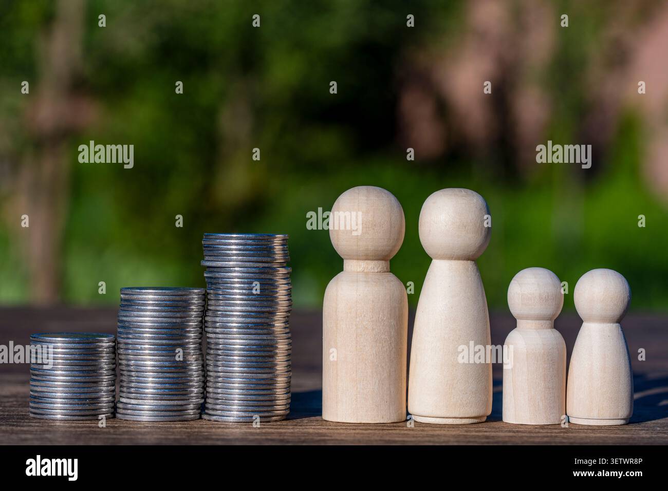 Tre pile crescenti di monete d'argento accanto a una famiglia simbolica di legno di quattro. Immagine concettuale per budget familiare, risparmi, pianificazione ipotecaria e f Foto Stock