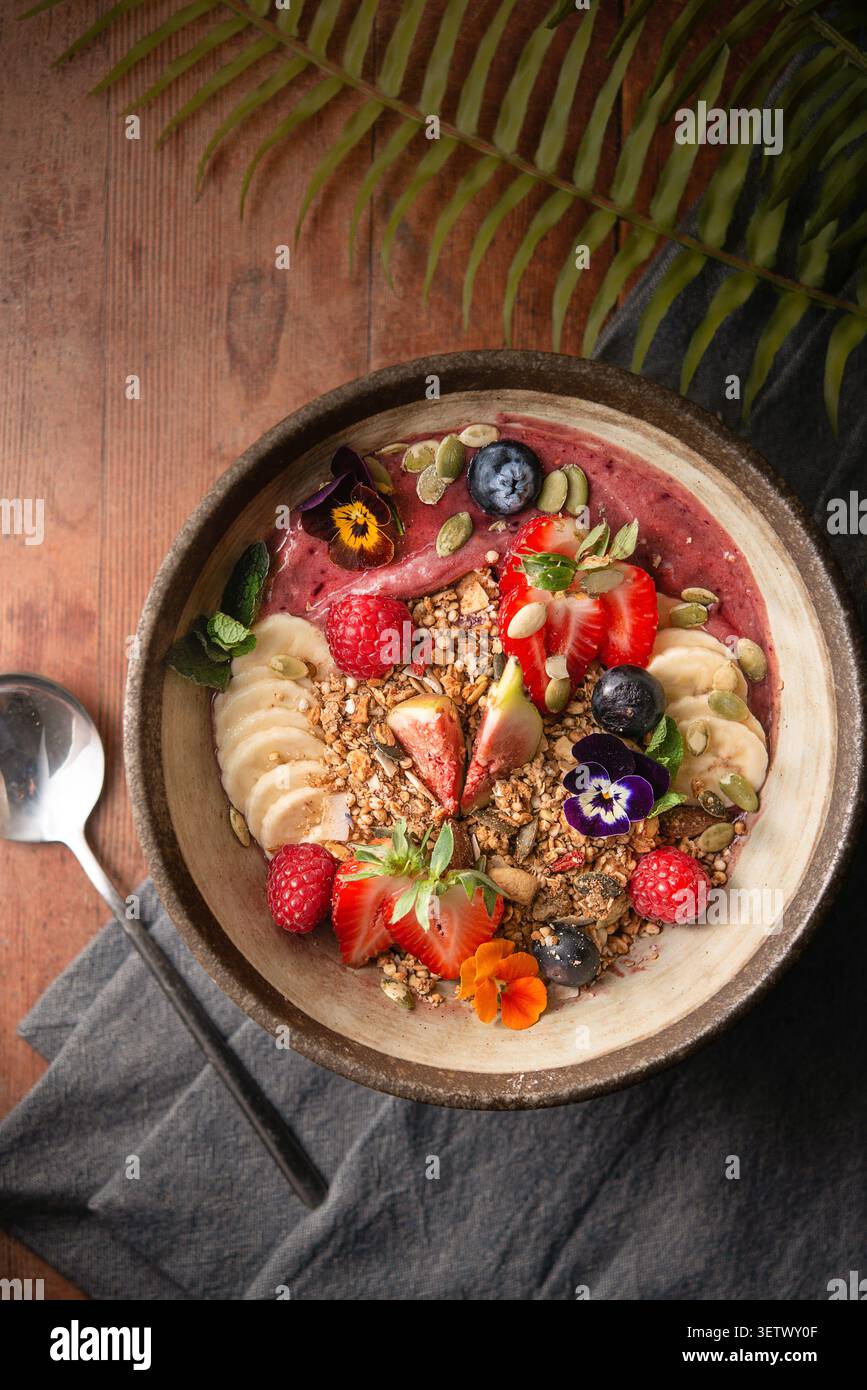 Vivace ciotola per frullati di acai condita con fragole fresche, fichi, banane, muesli e fiori commestibili. Foto Stock