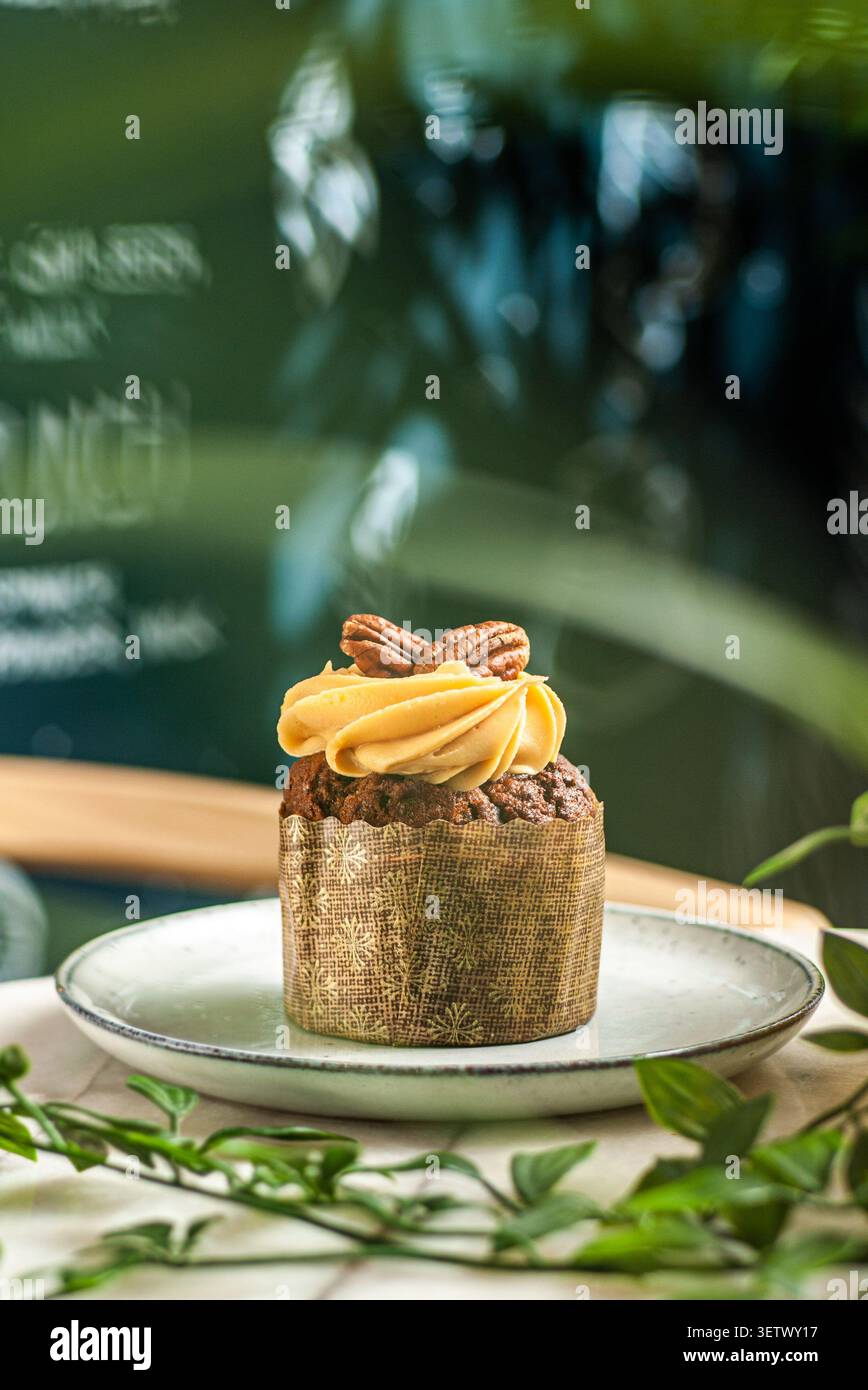 Un cupcake di spezie appena sfornato con una liscia glassa di caramello, ricoperto da metà di noci pecan intere su un piatto di ceramica. Foto Stock