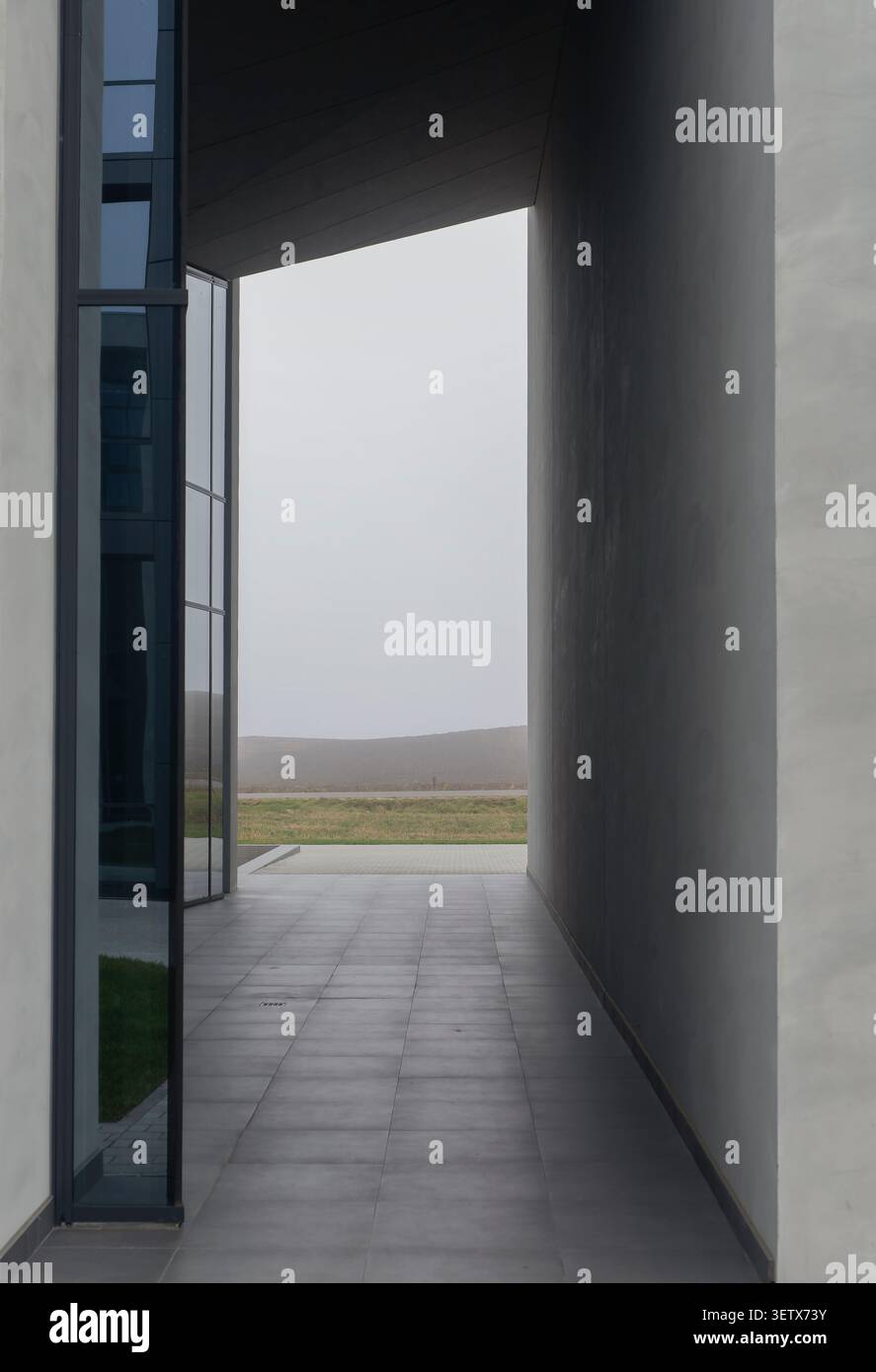 Passaggio architettonico tra pareti in cemento con apertura in vetro e vista prospettica. La struttura minima crea profondità e composizione spaziale. Concetto Foto Stock