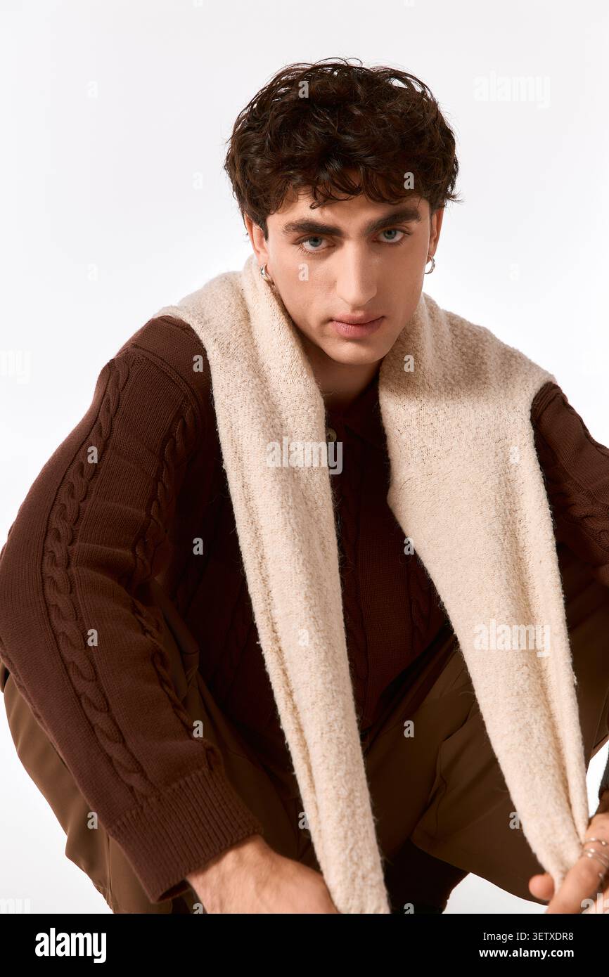 Un bell'individuo vestito con abiti alla moda pone con cura in uno spazio contemporaneo. Foto Stock