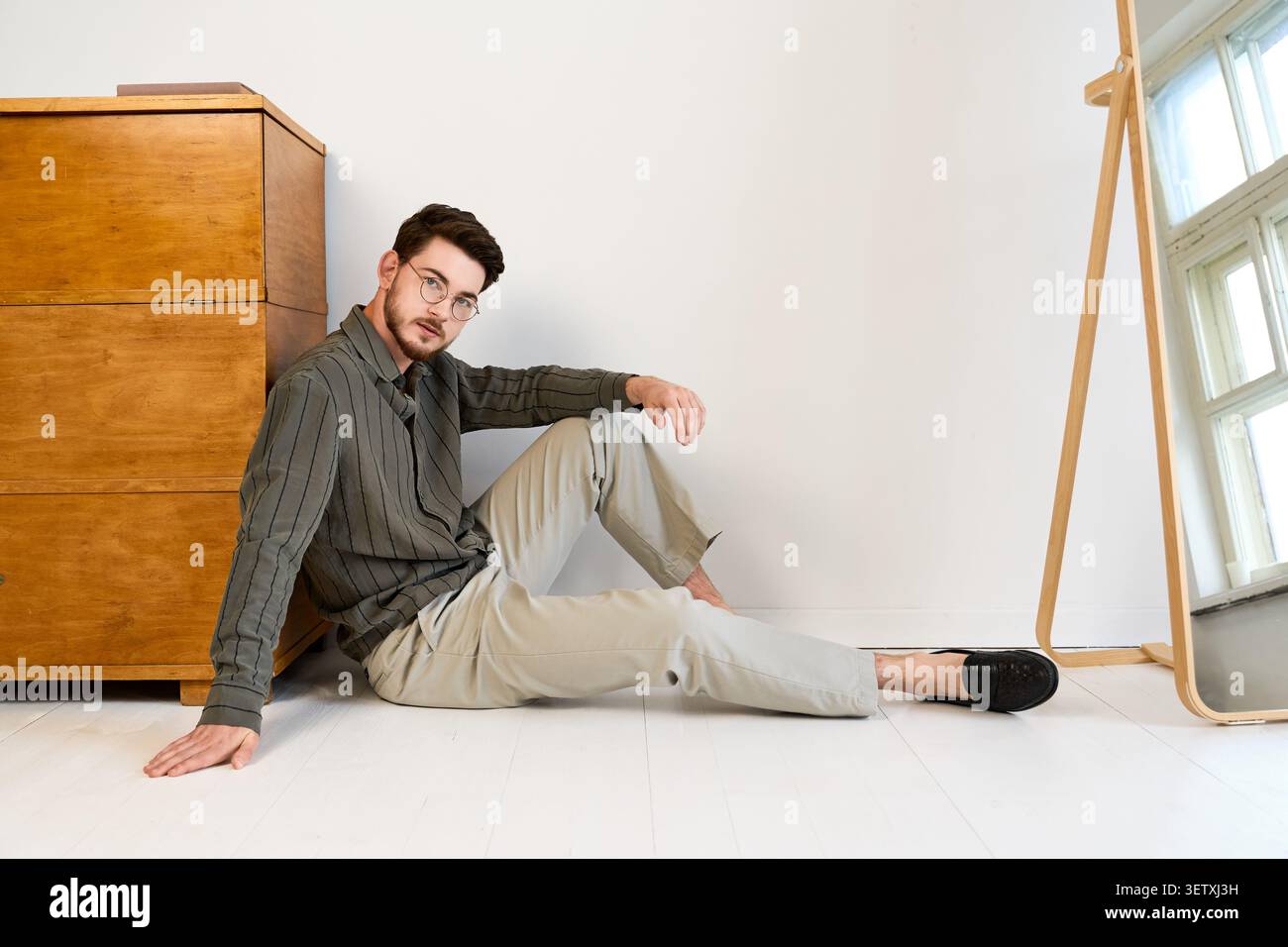 Il giovane con la barba in occhiali sfoggia un look casual e alla moda in uno spazio studio Foto Stock