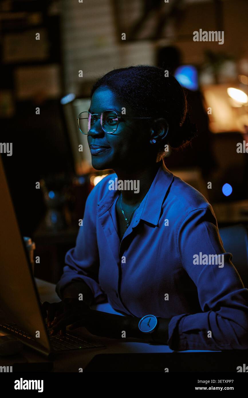 Donna adulta di colore che lavora su un notebook durante il turno di sera Foto Stock