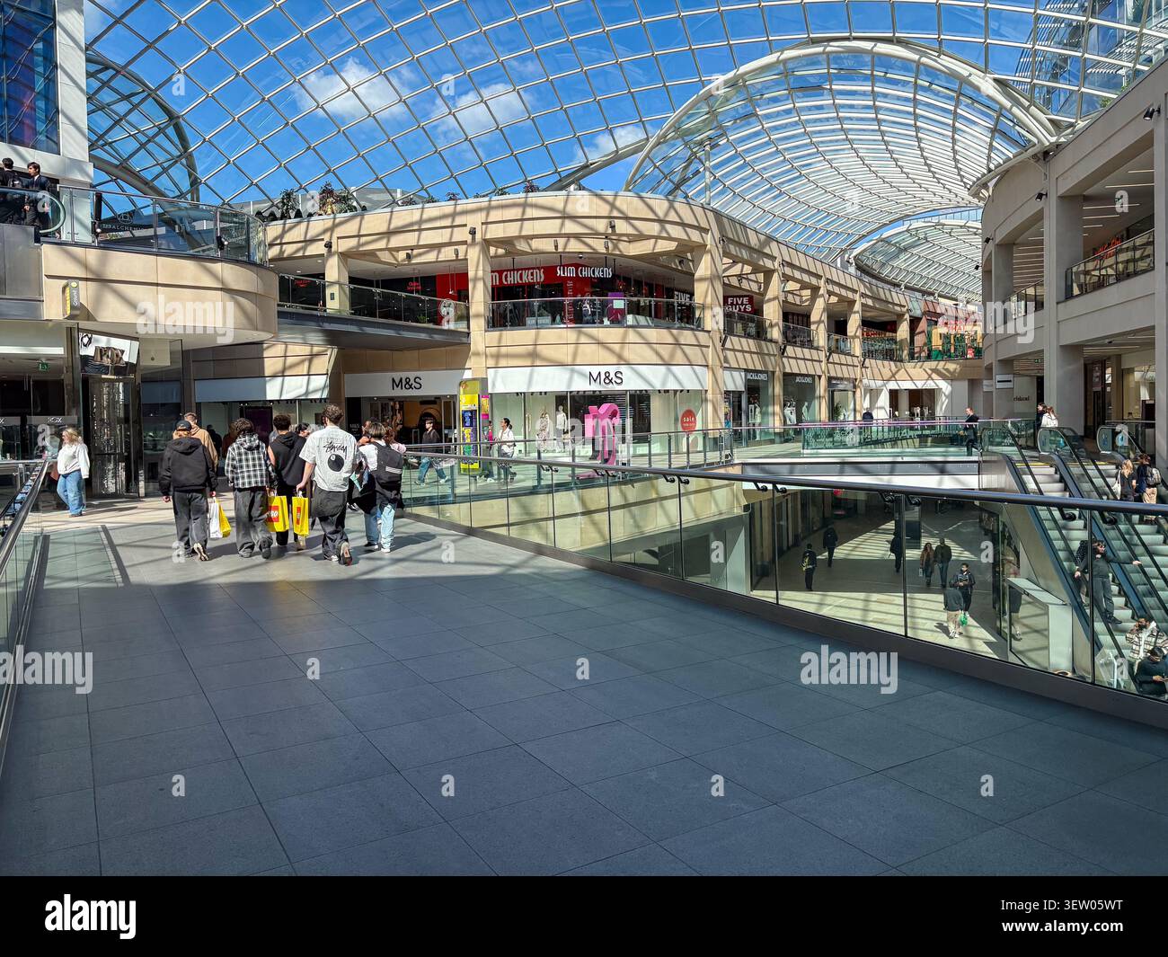 Gli amanti dello shopping camminano attraverso il moderno atrio con tetto in vetro del centro commerciale Trinity Leeds a Leeds, Regno Unito, con negozi al dettaglio e scale mobili. Foto Stock